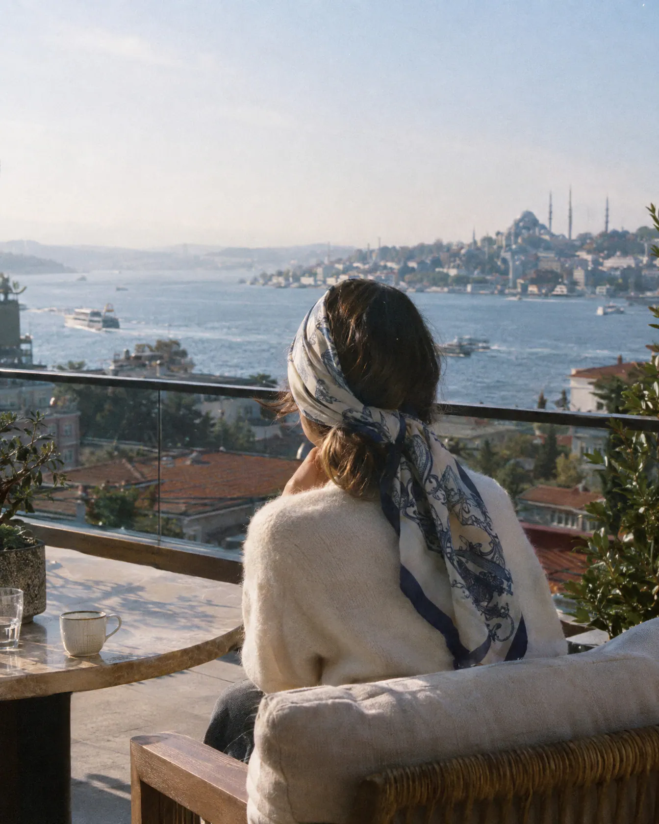 A woman with a silk scarf over her hair on a hotel terrace looking toward the Bosphorus