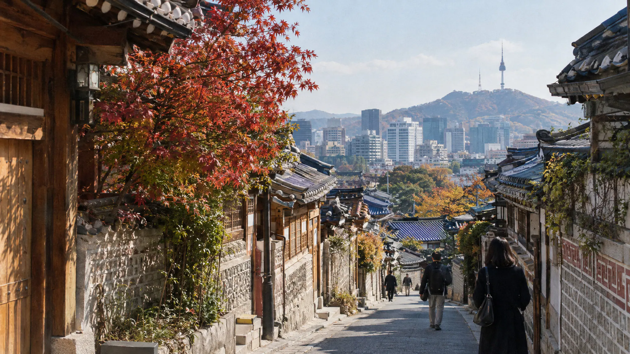 A sloping lane of hanok houses in Bukchon, Seoul, with autumn maples and the city behind