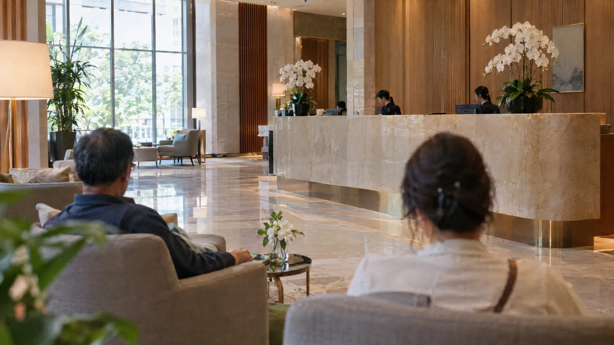 The daylit lobby of a modern private hospital in Bangkok with a stone reception desk and orchids